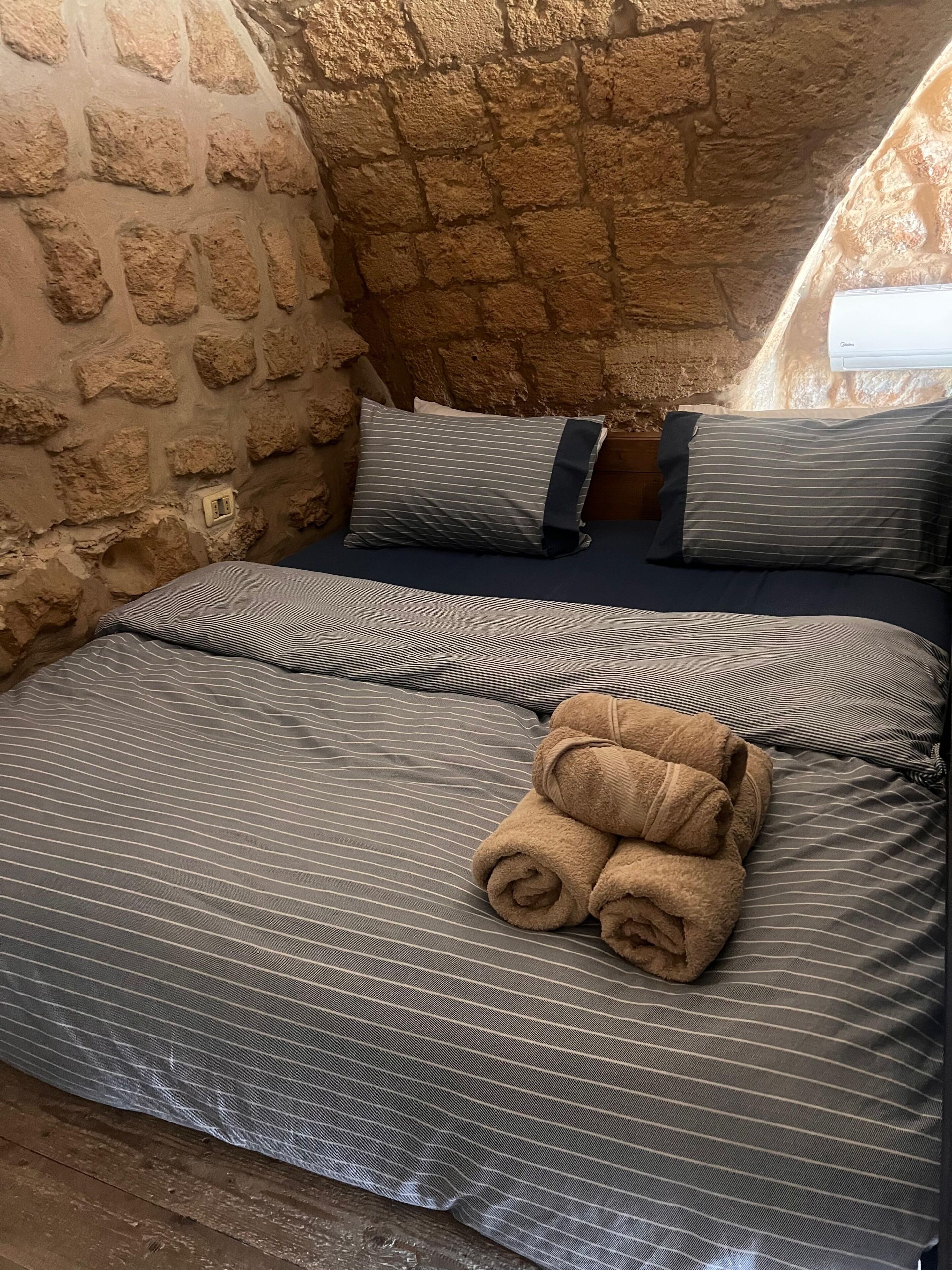Un dormitorio con pared de piedra, una cama con ropa de cama a rayas y dos almohadas.