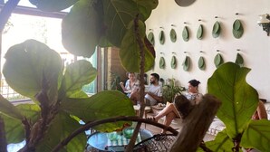 Ein Zimmer mit großen, grünen Blättern an der Wand, einem runden Tisch und Personen, die an ihm sitzen.