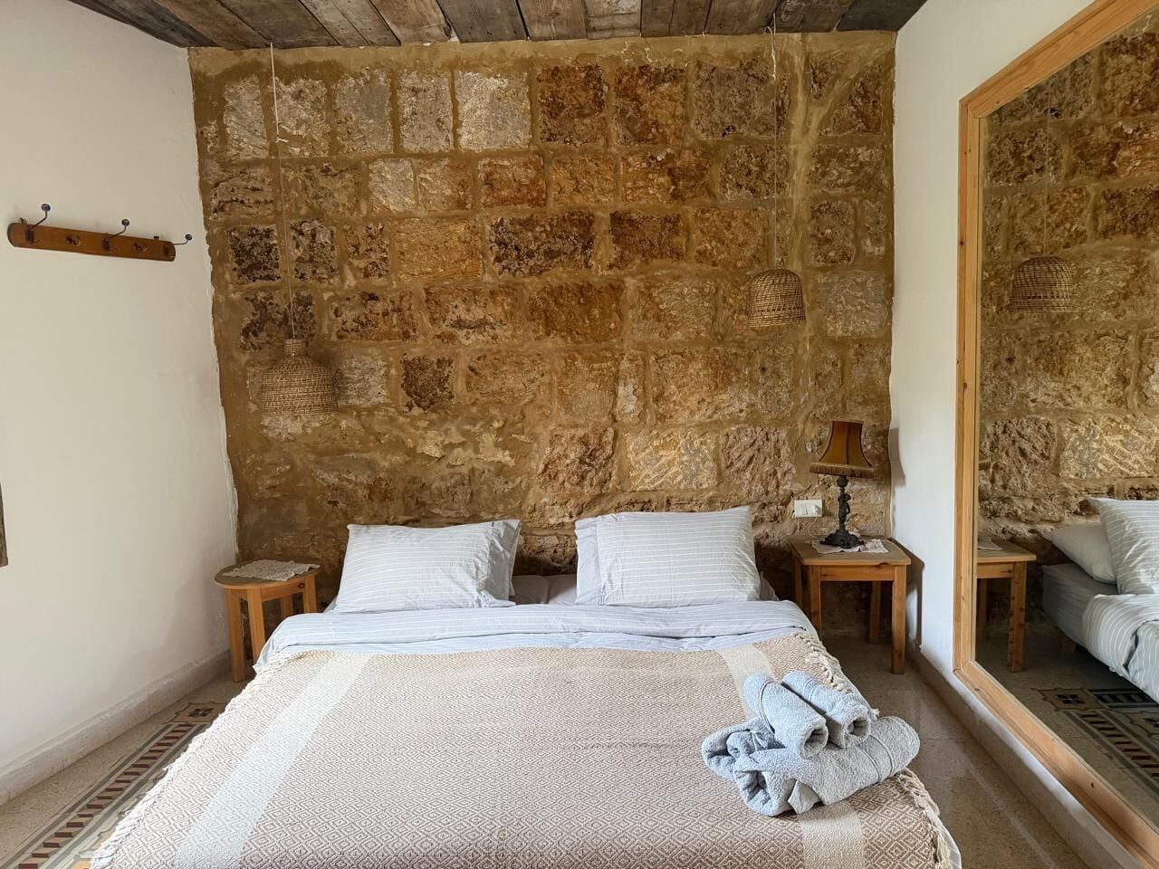 A bedroom with a stone wall, a bed with white linens, two bedside tables, and a mirror.