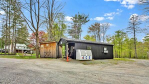 A rustic cabin with a small attached shed, surrounded by a gravel driveway and trees. - Full Hook up 30 Amp Site W Up to 26Ft (Wellsboro)