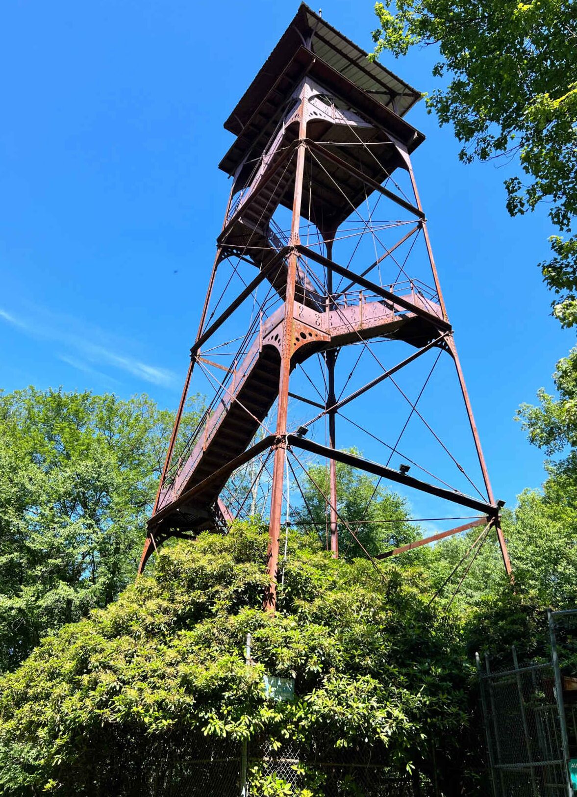 A tall, rusted metal structure with a staircase, surrounded by dense green foliage.