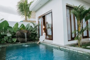 A pool with a waterfall, surrounded by lush greenery and a modern building with large windows. - Golden Bee (Mas)
