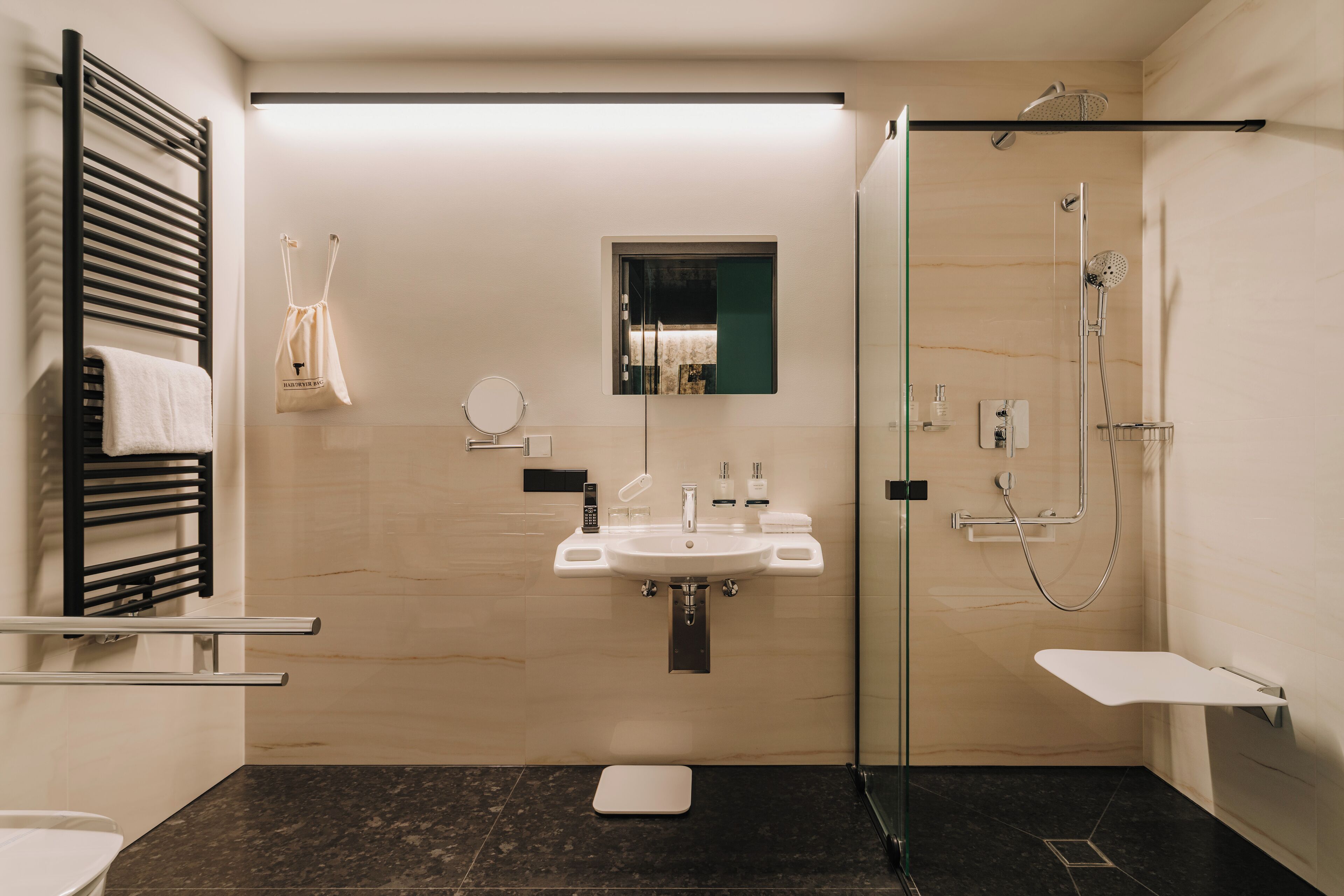 Un baño moderno con ducha envuelta en vidrio, un lavamanos blanco y un toallero negro.