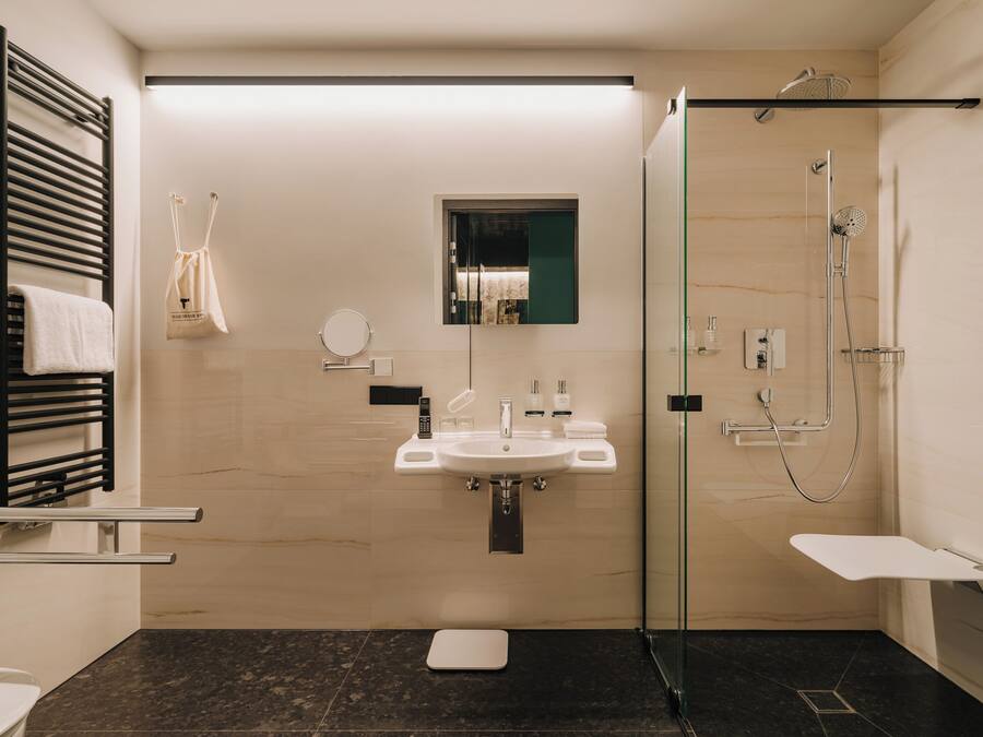 Un baño moderno con ducha envuelta en vidrio, un lavamanos blanco y un toallero negro.