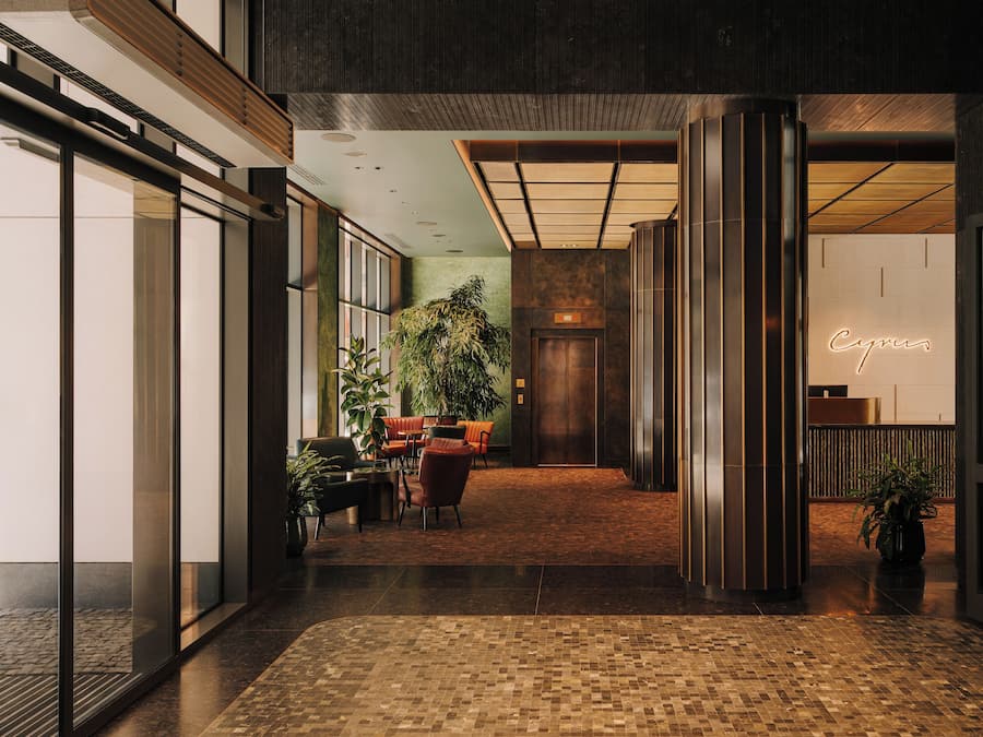 Un hall d’hôtel moderne avec un comptoir d’accueil, un espace salon et une grande plante en pot.