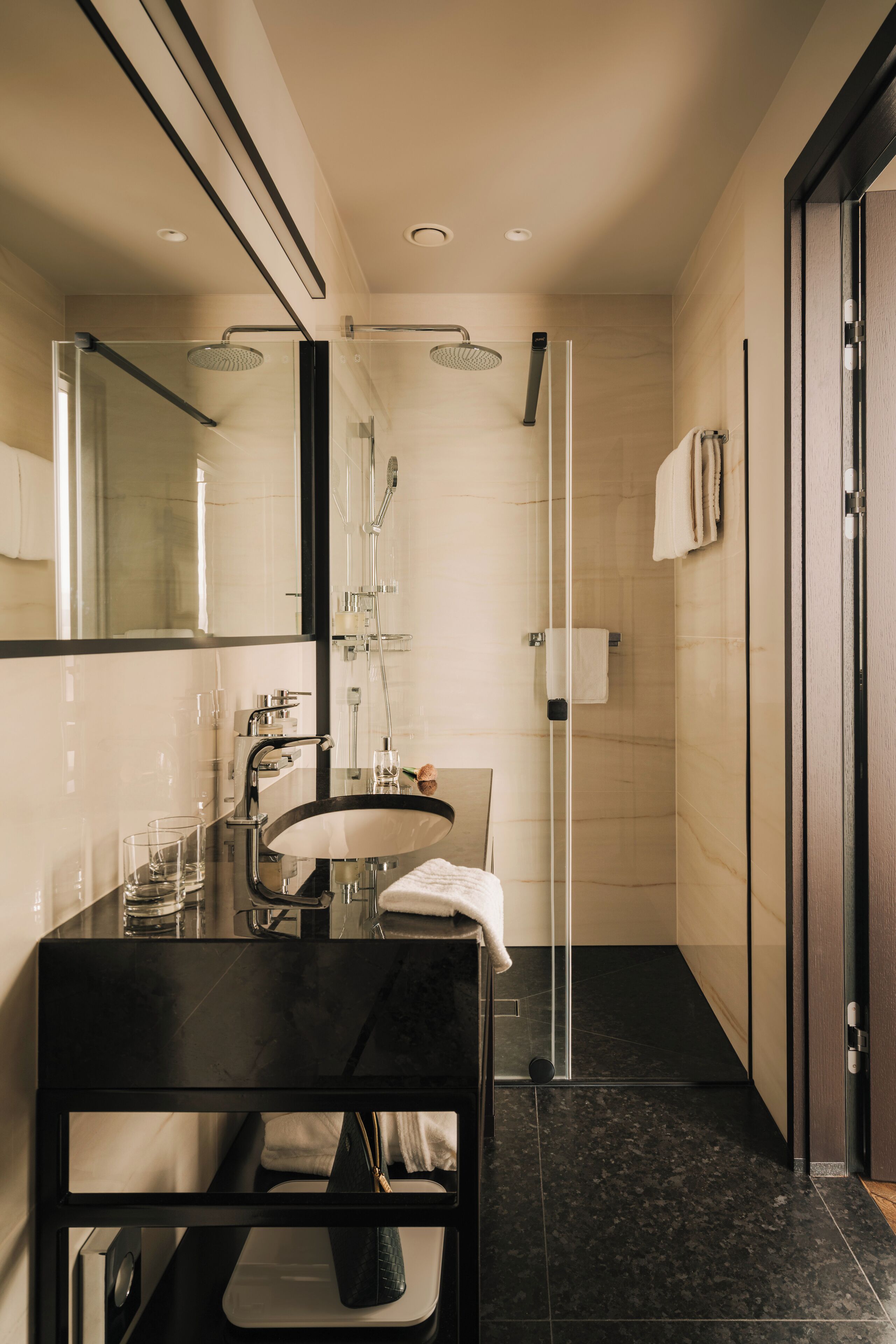 A modern bathroom with a glass shower enclosure, a black vanity, and a large mirror.