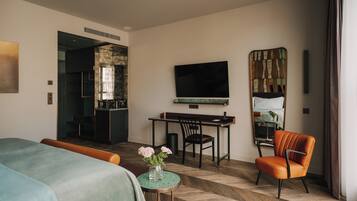 A hotel room with a bed, a desk, a chair, a TV, and a small table with flowers.