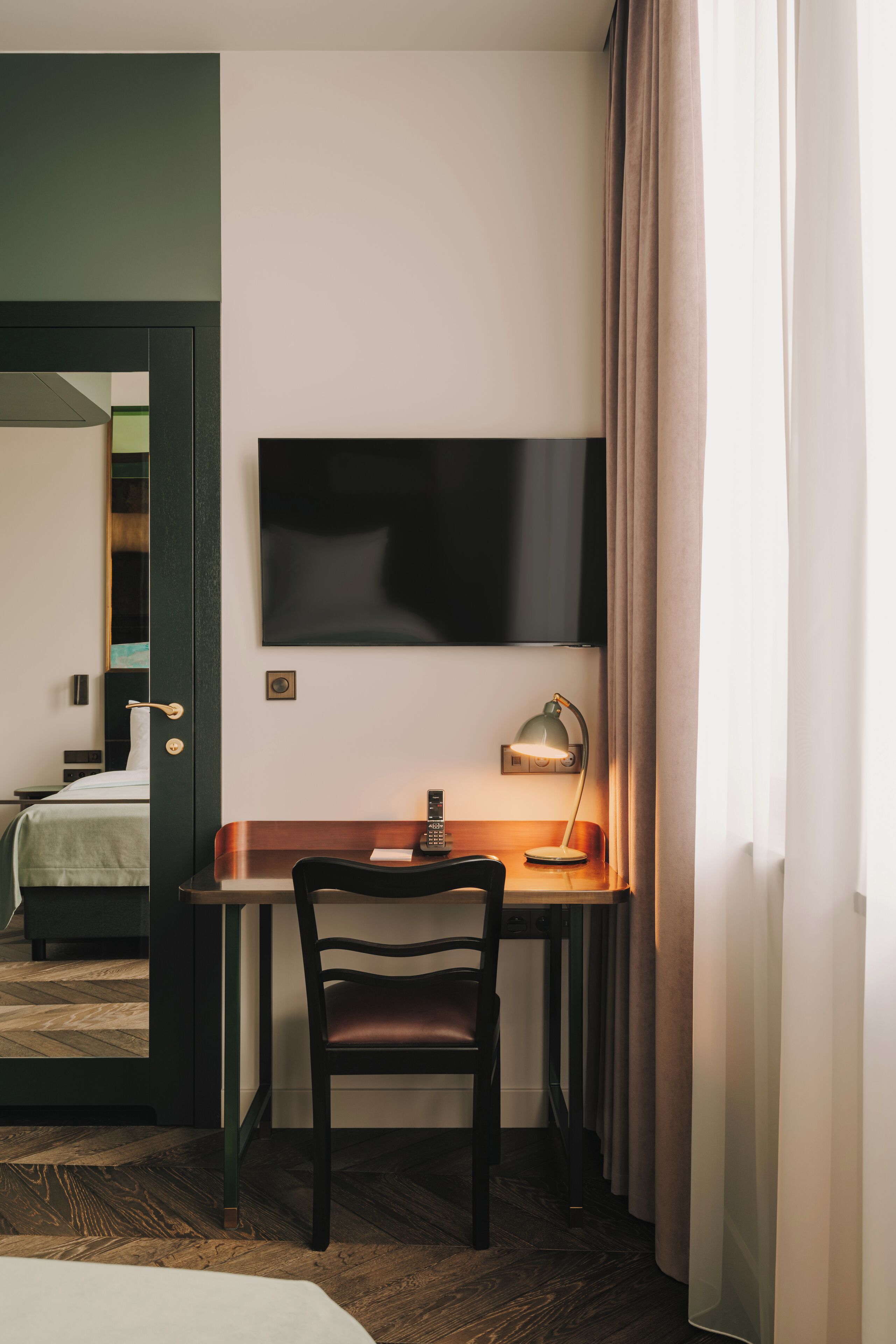 A hotel room with a desk, chair, and a flat-screen TV mounted on the wall.