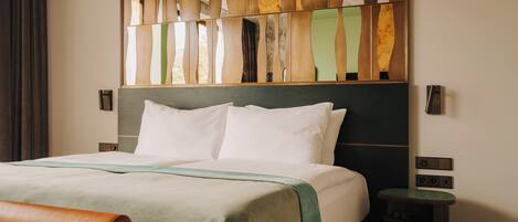 A neatly made bed with white linens, a green and brown bedspread, and a wooden headboard with a decorative panel.