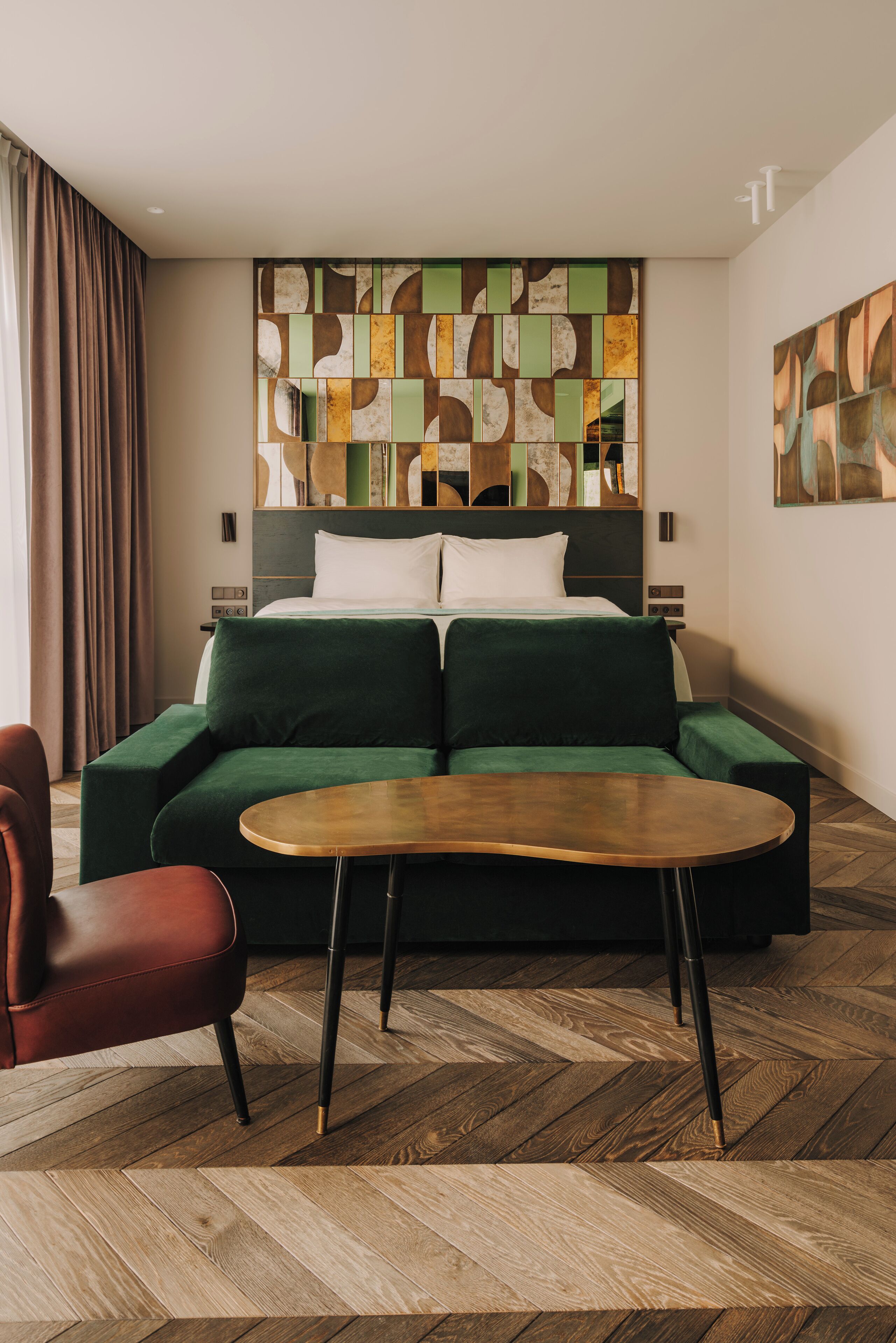 Une chambre d’hôtel moderne avec un grand lit, un canapé vert, une table basse en bois et un fauteuil rouge.