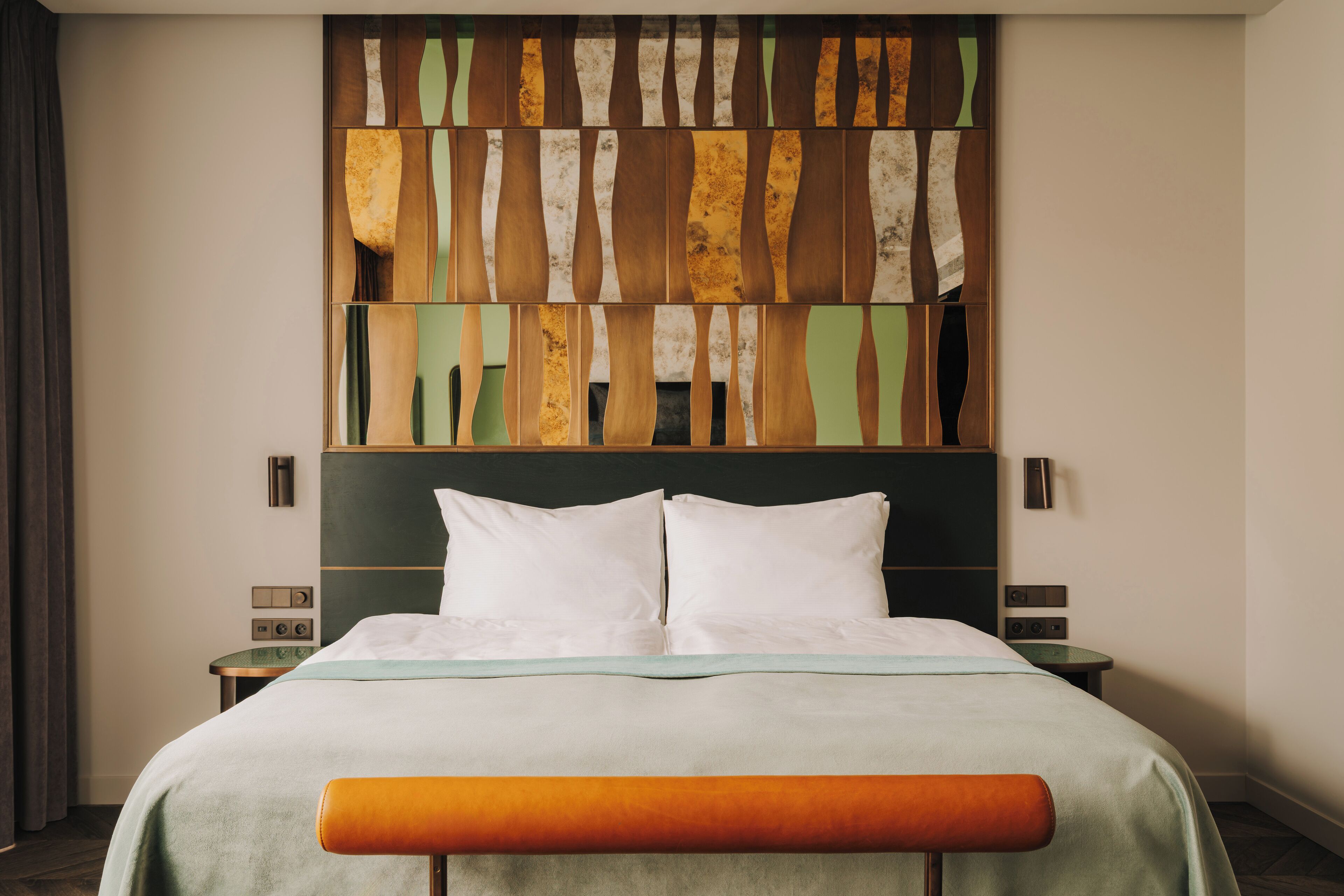 Una habitación de hotel con cama, un banco, una mesita de noche y una obra de arte en la pared.