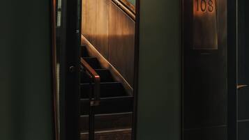 Un espejo refleja una escalera de madera y un panel de control de ascensor fijado a la pared con el número 108.