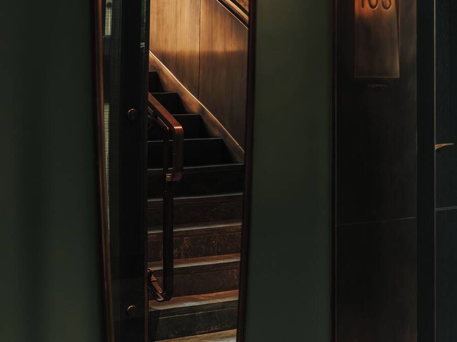 Un espejo refleja una escalera de madera y un panel de control de ascensor fijado a la pared con el número 108.