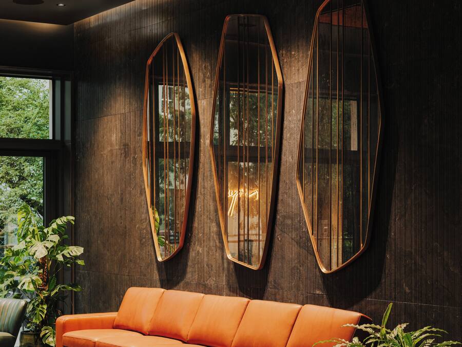 A modern interior with a leather sofa, large mirrors, and potted plants.