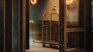 A hotel lobby with a glass door, a luggage cart, and a circular light fixture. - The Cyrus Hotel (Wroclaw)