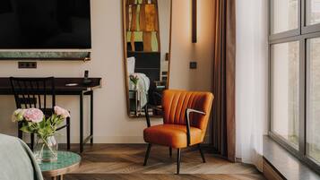Una habitación de hotel moderna con un ventanal grande, un televisor de pantalla plana, una mesa de comedor con sillas y un espejo decorativo.