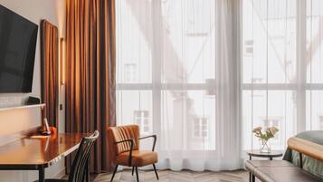 Et moderne hotelværelse med trægulv i fiskebensmønster, et fladskærms-tv, et skrivebord med stol, en sofa og en bænk.
