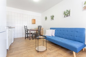 En moderne stue med en blå sofa, et spisebord med stole, et køkkenområde og et flisebeklædt backsplash.
