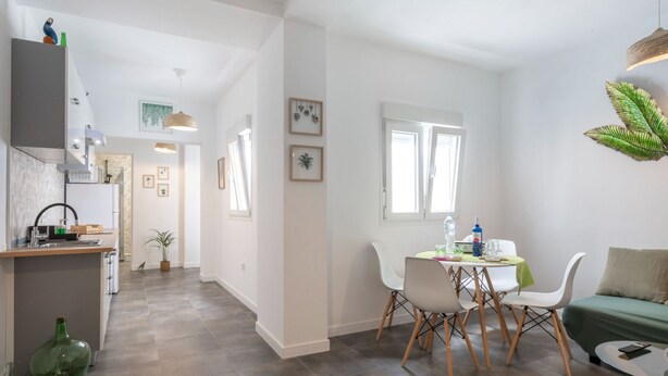 A modern kitchen with a built-in oven, a dining area with a table and chairs, and a living area with a sofa and a plant. - Jardín: Cómodo y Luminoso Apartamento (Santa Cruz de Tenerife)