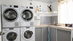 A laundry area with stacked front-loading washers and dryers, a sink, and shelves with cleaning supplies. - Jardín: Cómodo y Luminoso Apartamento (Santa Cruz de Tenerife)