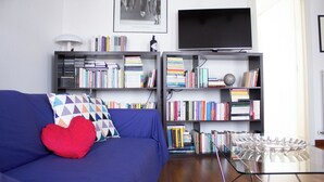 A living room with a blue sofa, heart-shaped pillow, and two bookshelves filled with books. - Passons 4 - One Bedroom Apartment, Sleeps 2 (Udine)