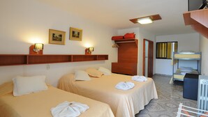 A hotel room with two beds, a wooden shelf with framed pictures, a red storage unit, and a bunk bed in the background. - Hotel de la Cuesta (Villa Carlos Paz)