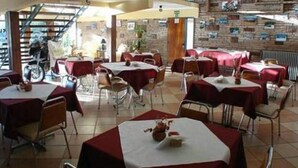 A dining area with tables covered in red tablecloths, chairs, and a brick wall in the background. - Hotel de la Cuesta (Villa Carlos Paz)