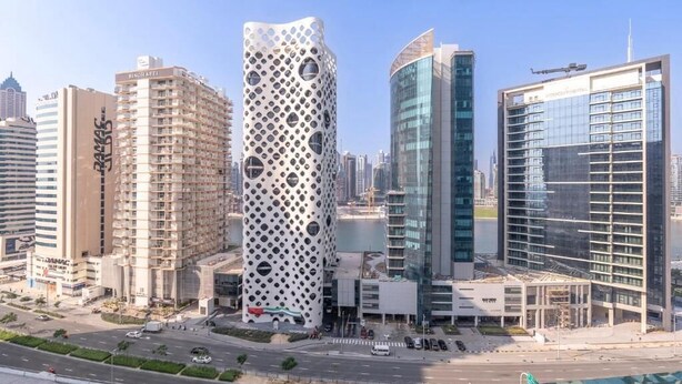Un paisaje urbano moderno con un edificio distintivo que cuenta con una fachada perforada, rodeado de otros edificios altos.