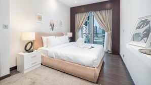 Un dormitorio moderno con una cama grande, mesitas de noche y vistas de la ciudad a través de la ventana, con un paisaje urbano visible.