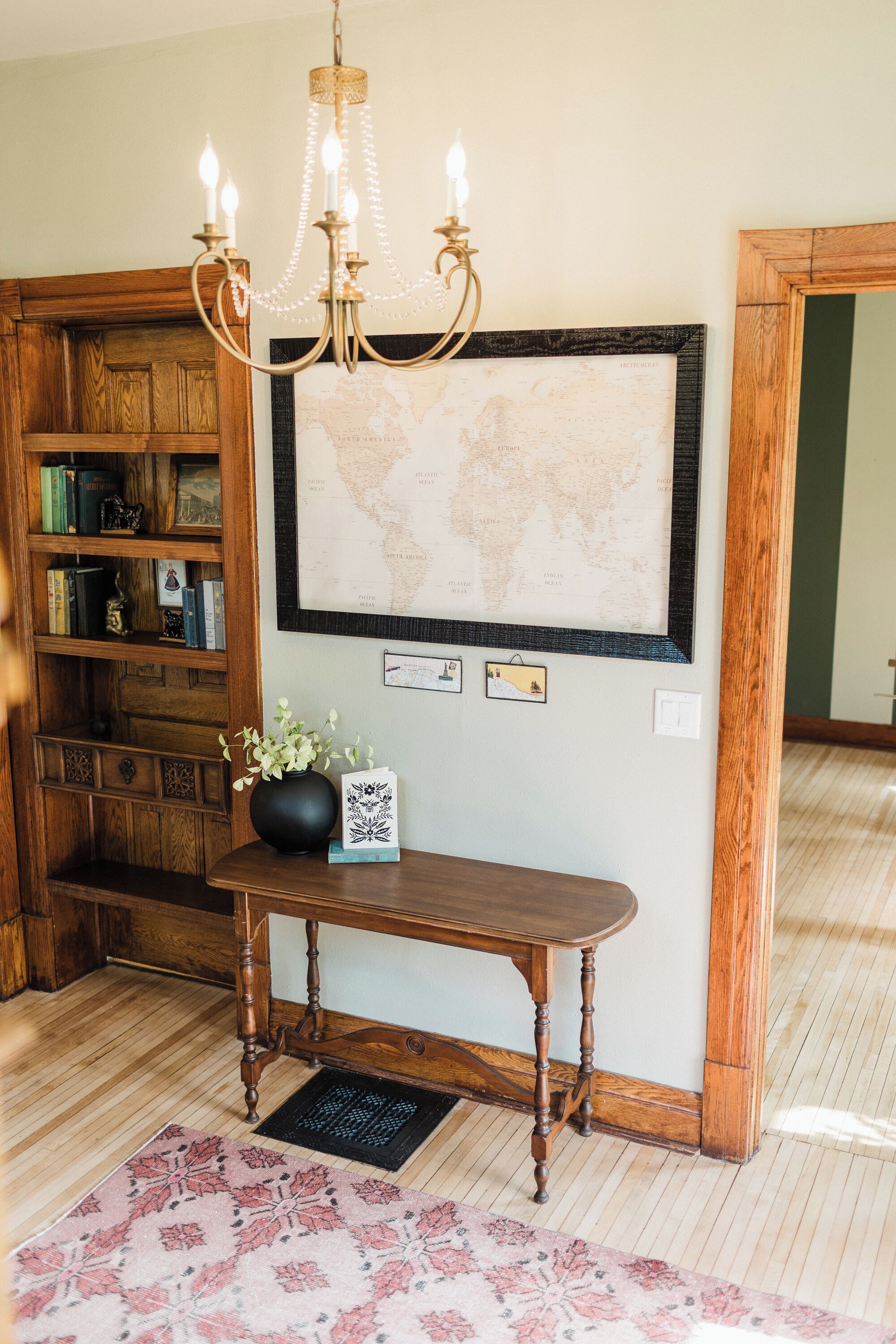 A wooden console table with a world map, a chandelier, and a bookshelf with books and decorative items.