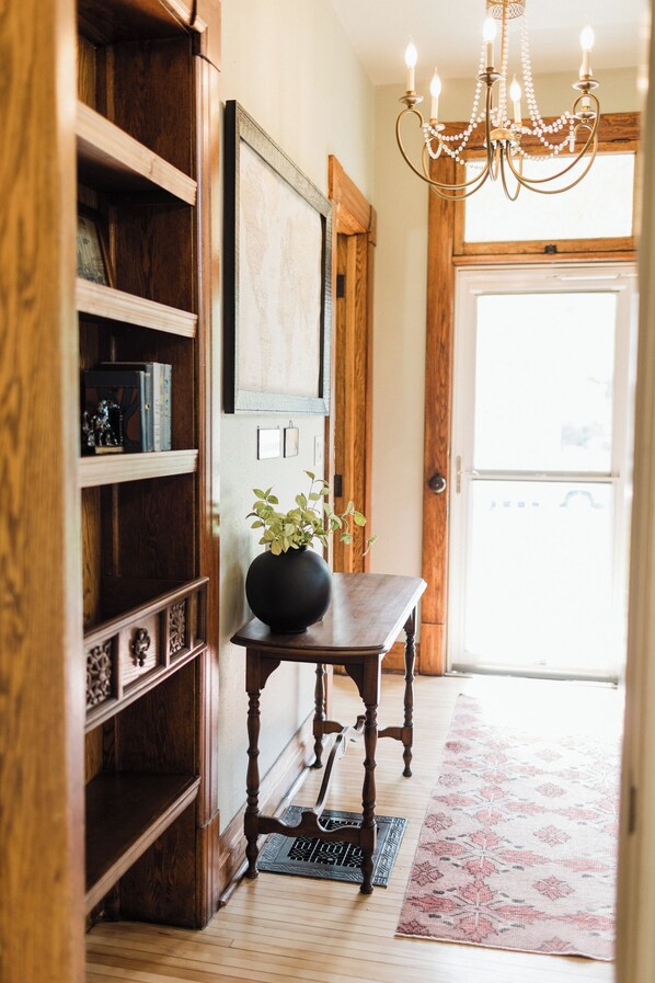 Une bibliothèque en bois, un vase noir avec une plante, une table en bois et un tapis à motifs dans un couloir.