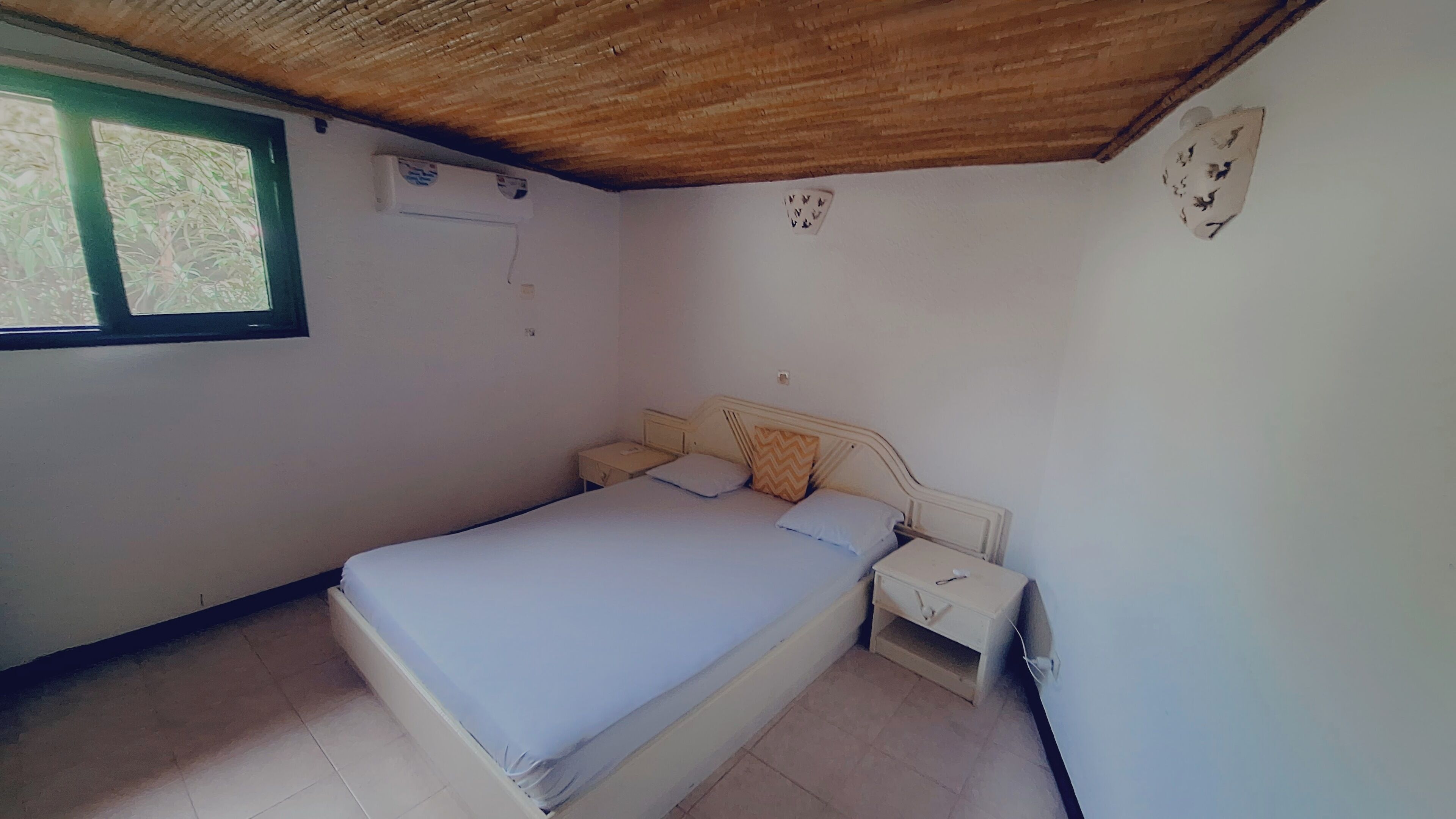 A bedroom with a single bed, a nightstand, a window with a view, and a wooden ceiling.