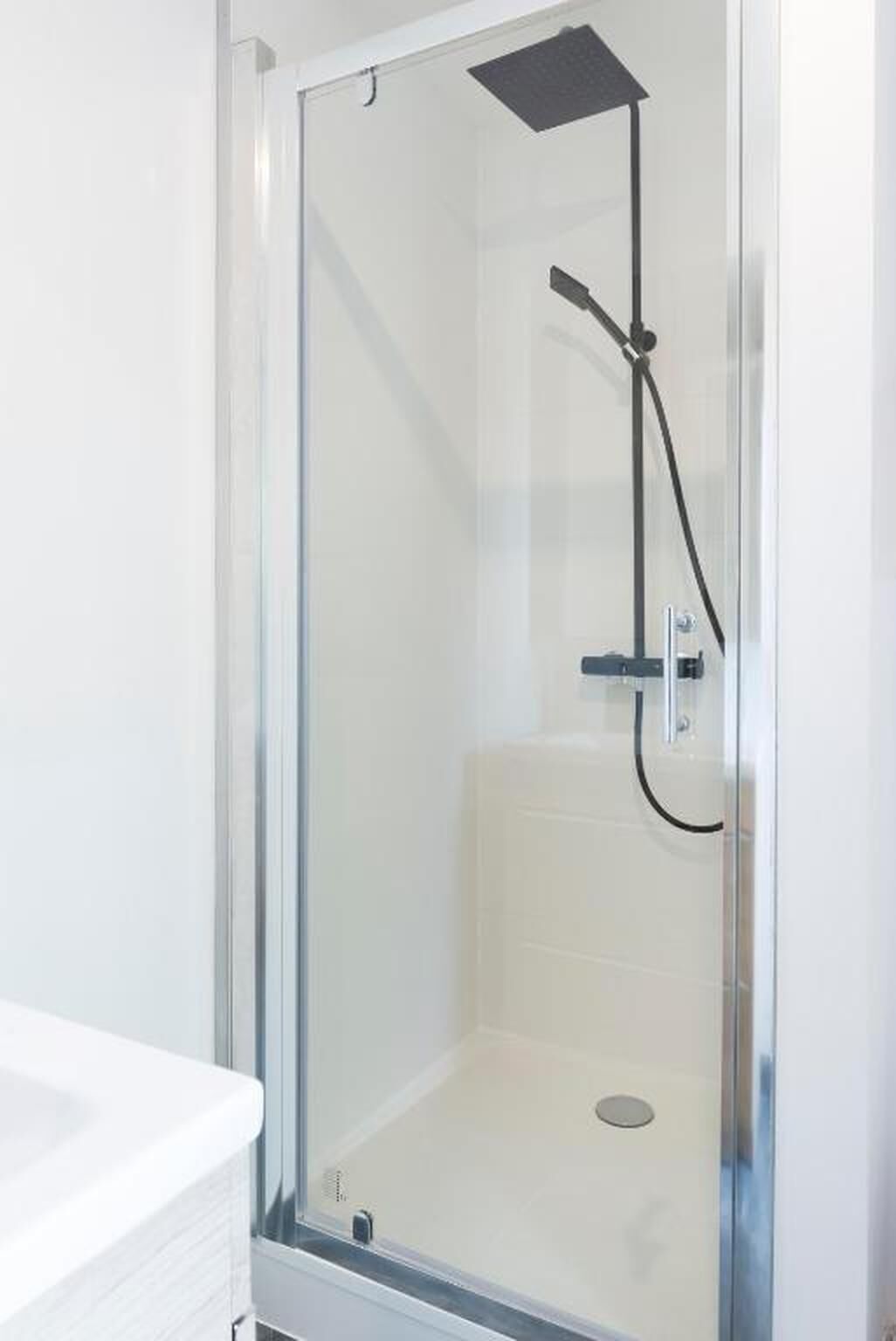 A glass-enclosed shower with a black showerhead and handle.