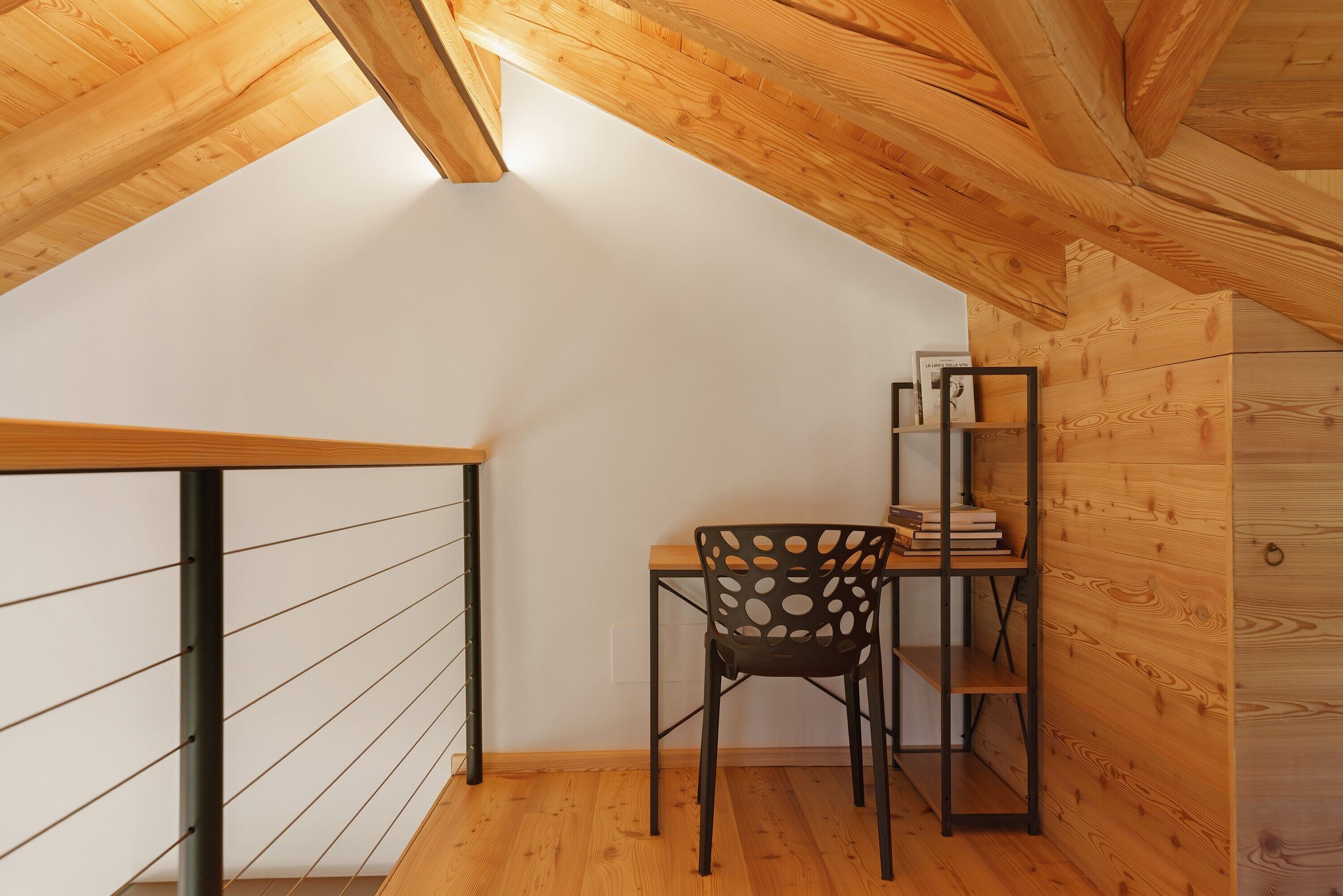 A small room with a sloped ceiling, a desk with a chair, a bookshelf, and a wooden wall.