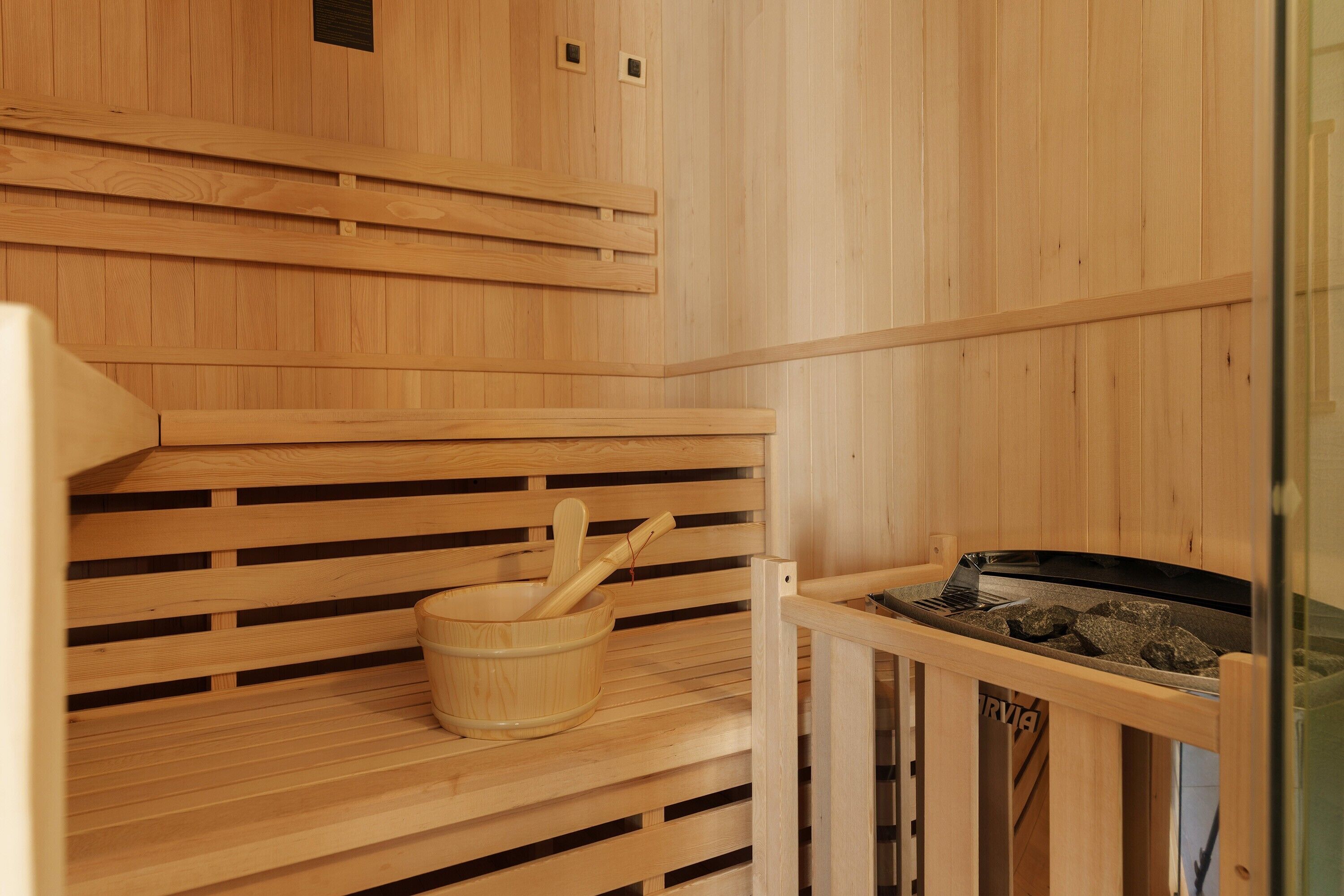 A wooden sauna with benches, a wooden bucket, and a sauna heater.
