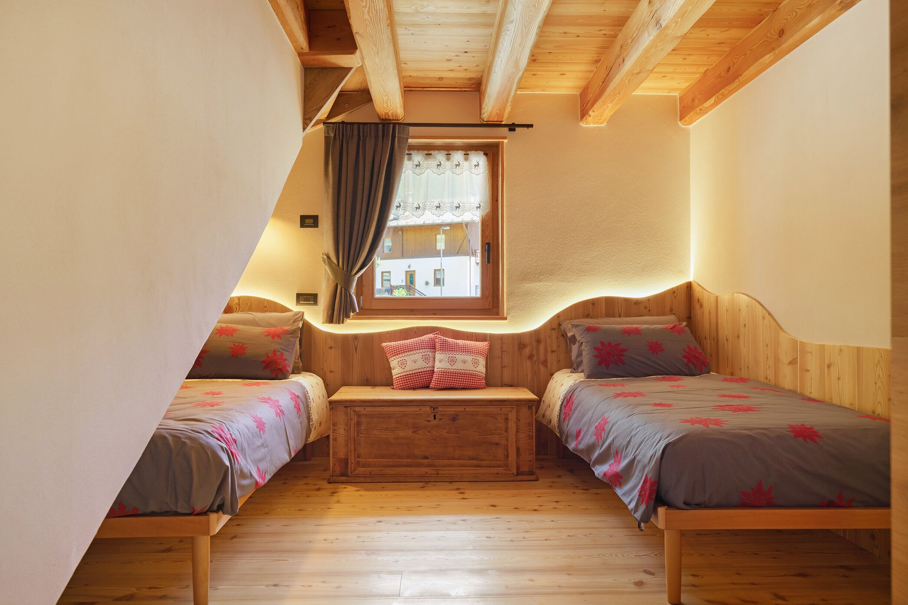 Ein Zimmer mit zwei Holzbett, einer Bank und einem Fenster mit Vorhängen.