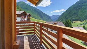 A wooden balcony with a view of a mountain landscape and houses.