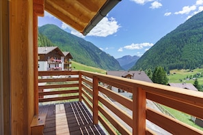Un balcón de madera con vistas a un paisaje montañoso y casas.