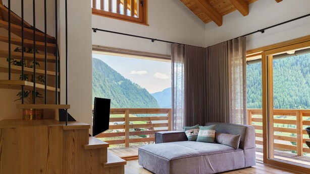 A modern room with a wooden staircase, a sofa, a TV, and large windows with a mountain view.