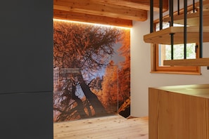 Un interior de madera con una escalera, un ventanal y un mural de un árbol en la pared.