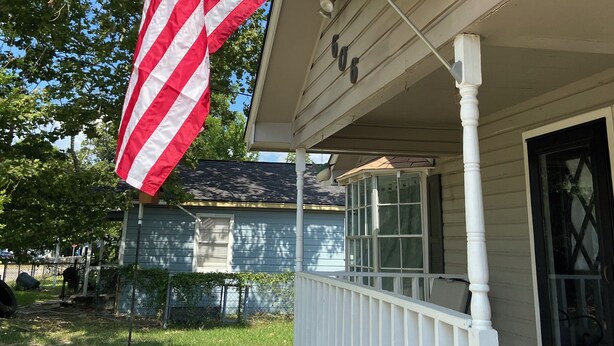 A house with a porch, a flagpole with an American flag, and a window with a lattice design.