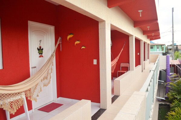 A red building with a white door, a hammock, and a red chair on the porch. - Pousada Residencial La Puerta Del Sol (Ipojuca)