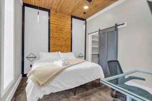 A modern hotel room with a bed, a glass table, and a sliding door closet. - Walk to Downtown, King Bed, great for long stays (Spartanburg)