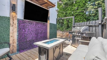 Une terrasse extérieure dotée d’un foyer intégré, d’un barbecue et d’un espace salon confortable avec des coussins.