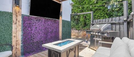 An outdoor patio with a built-in fire feature, a barbecue grill, and a cushioned seating area.