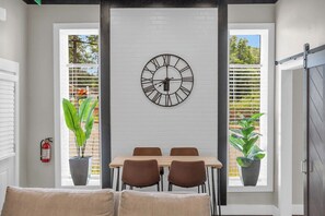 A dining area with a wall-mounted clock, a table with chairs, and potted plants. - Industrial Loft - Walk to Downtown, Patio w/ BBQ (Spartanburg)