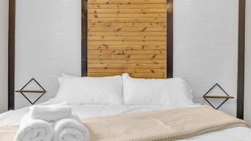 A bed with white bedding, a beige blanket, and rolled white towels.