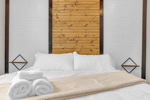 A bed with white bedding, a beige blanket, and rolled white towels.
