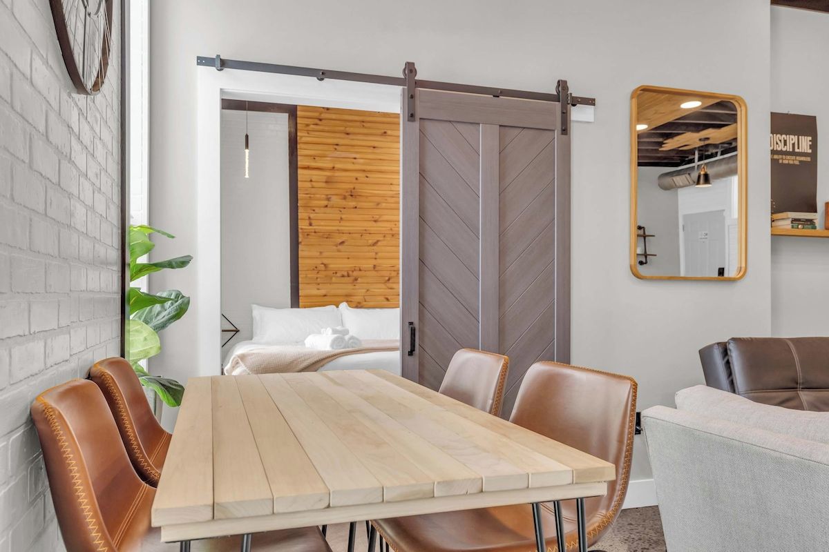 Un interior moderno con una mesa de madera, sillas de cuero, una puerta corredera estilo granero, un espejo y una planta.