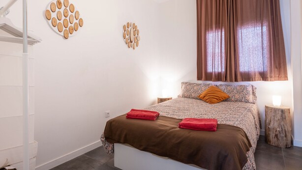 A bedroom with a bed, two wall decorations, a window with curtains, and a bedside table.